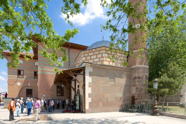 Ein historisches Gebäude mit einer Kuppel und Bogenfenstern, umgeben von Bäumen und blauem Himmel.
