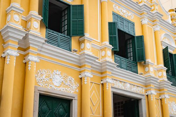 A yellow building with green shutters and white decorative moldings.