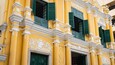 A yellow building with green shutters and white decorative moldings.