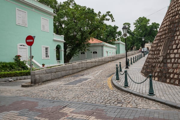 A cobblestone street with historic buildings, a 'no entry' sign, and a stone wall.