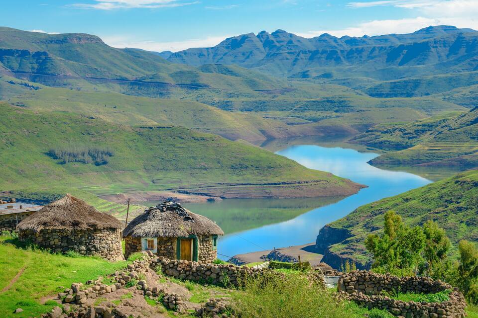 A mountainous landscape with a lake, stone houses, and a thatched-roof hut.