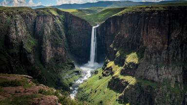 A waterfall cascading down a steep gorge surrounded by lush green hills.