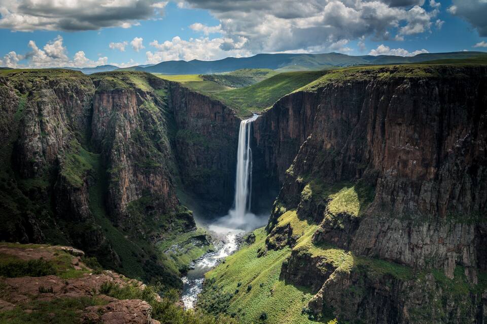 A waterfall cascading down a steep gorge surrounded by lush green hills.