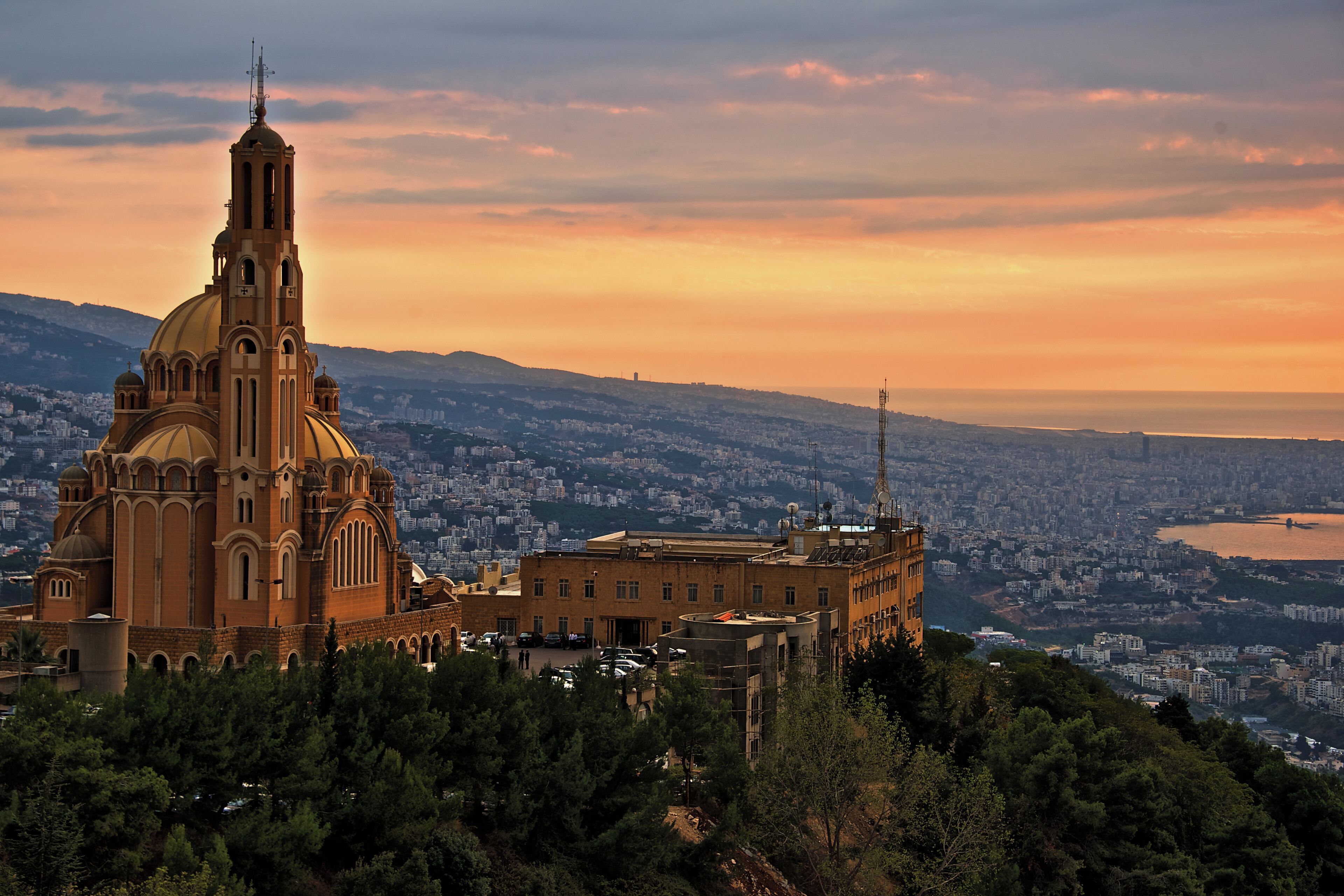 A large church with a prominent dome and bell tower, surrounded by dense trees and a cityscape in the background.