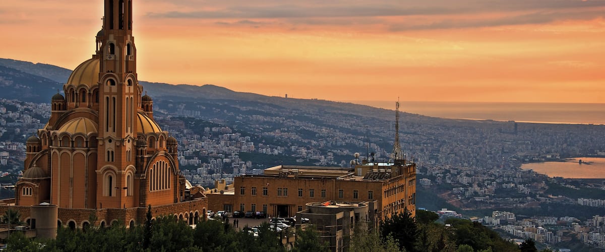 A large church with a prominent dome and bell tower, surrounded by dense trees and a cityscape in the background.