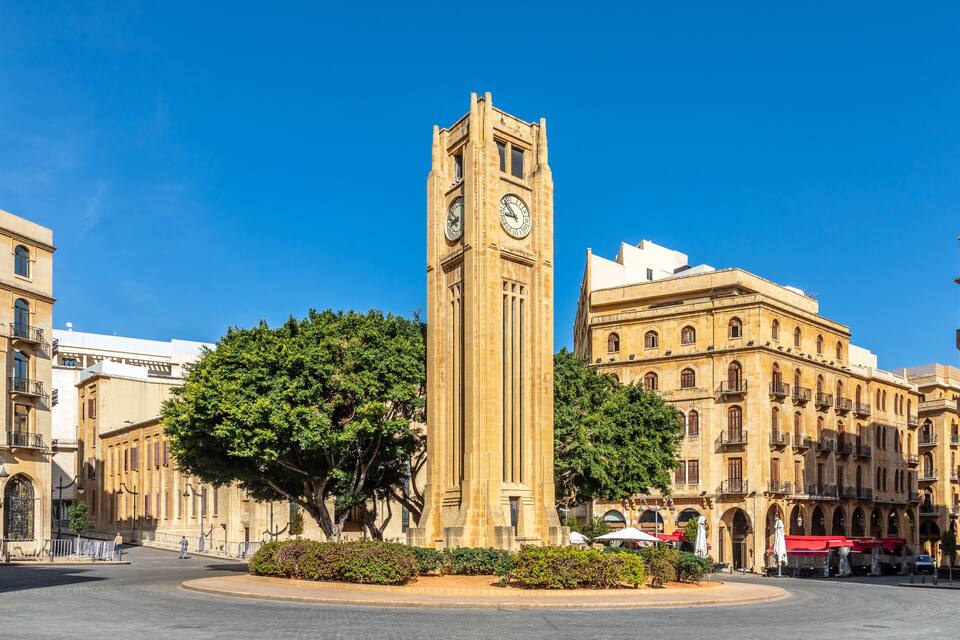 A historic clock tower in a city square surrounded by classic architecture.