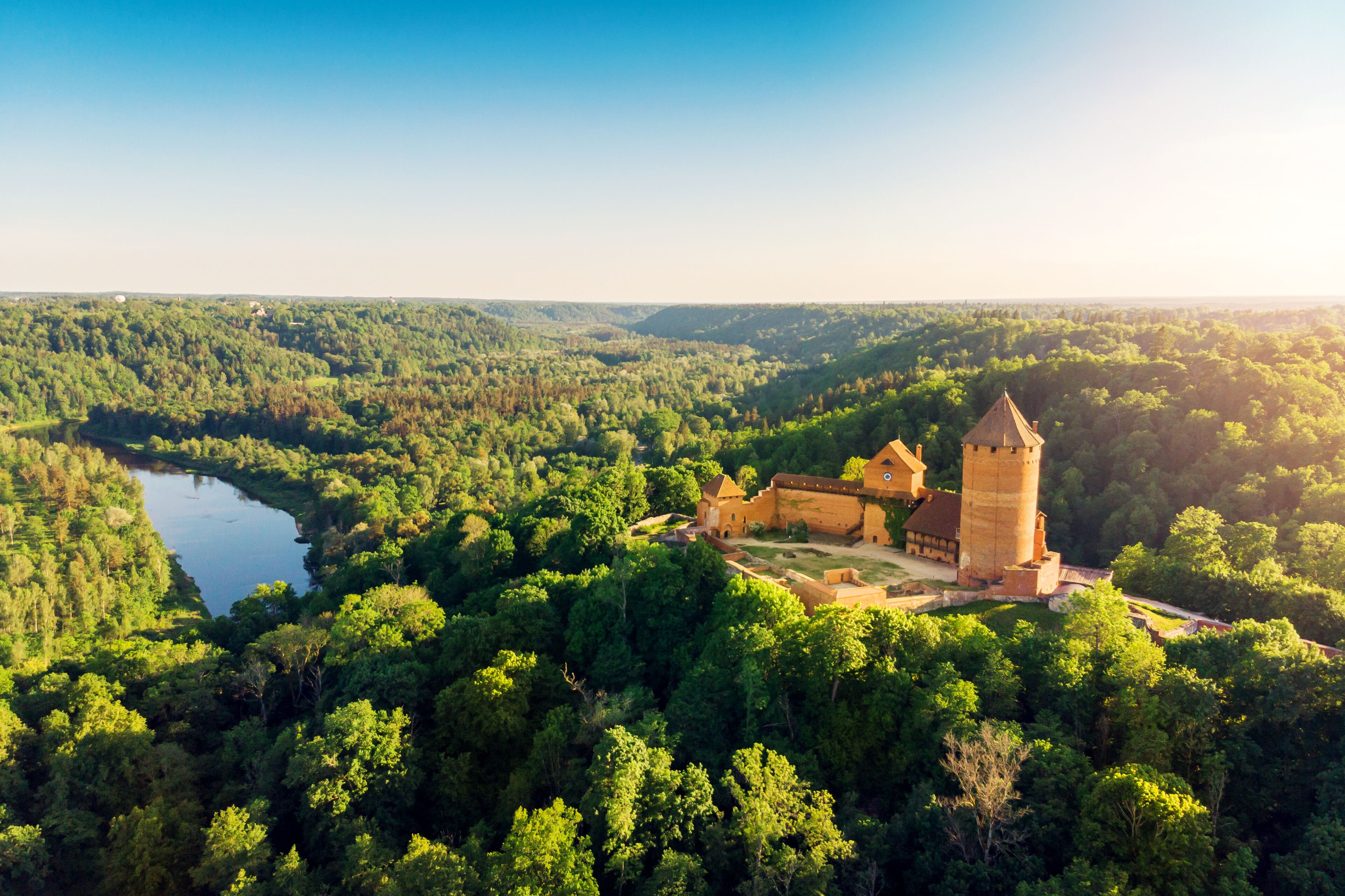 A castle surrounded by dense forest and a river.