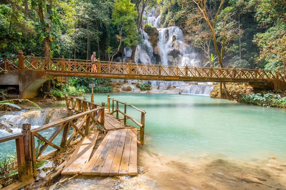 A wooden bridge over a river with a waterfall in the background.