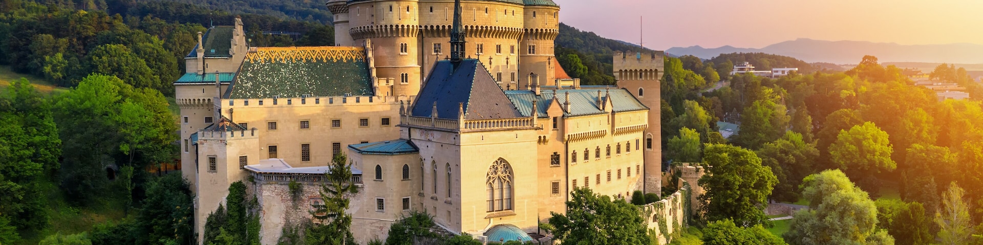 A castle with multiple towers, surrounded by lush greenery and a river.