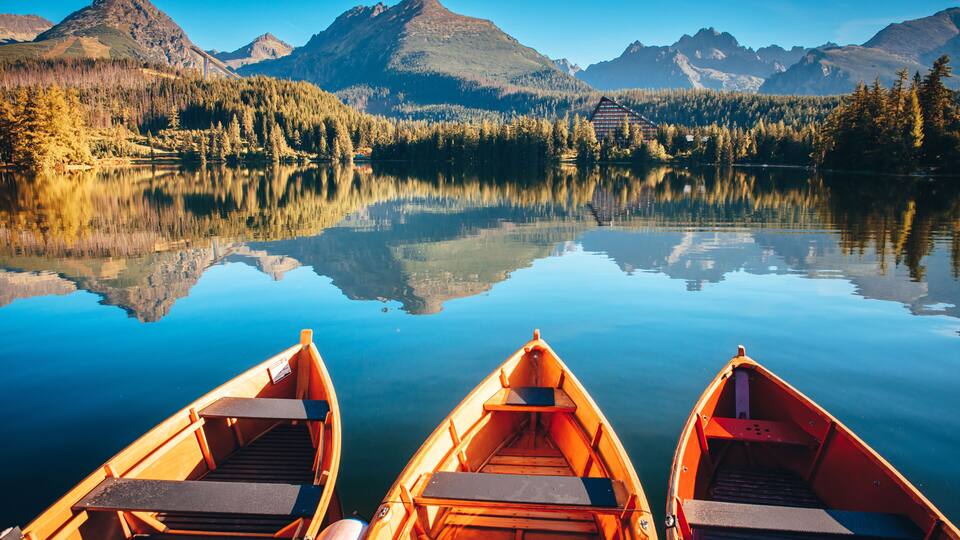 A calm lake with reflections of mountains and a cabin, surrounded by forest.