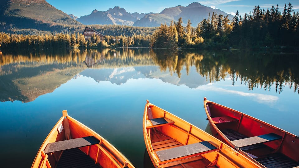 Two wooden boats on a calm lake with reflections of mountains and trees.
