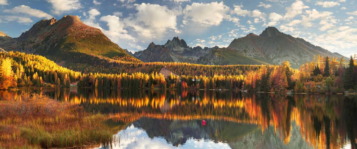 A mountain range with autumn foliage, a lake reflecting the scenery, and a bridge in the distance.