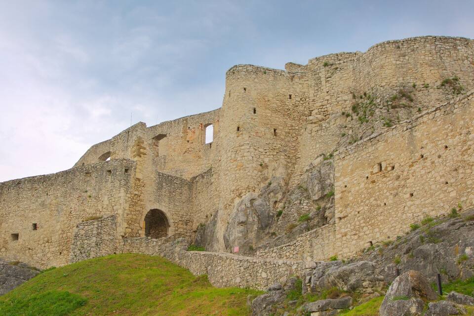 A historic stone fortress with multiple arches and a grassy hill in the foreground.