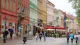 A cobblestone street lined with colorful buildings, flags, and outdoor cafes.
