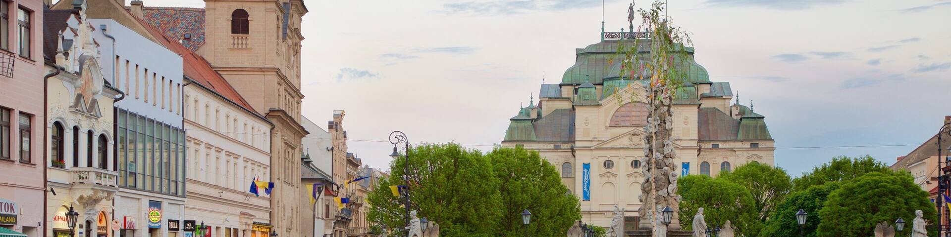 A cobblestone square with a tram track, historic buildings, and a large ornate church with a green dome.