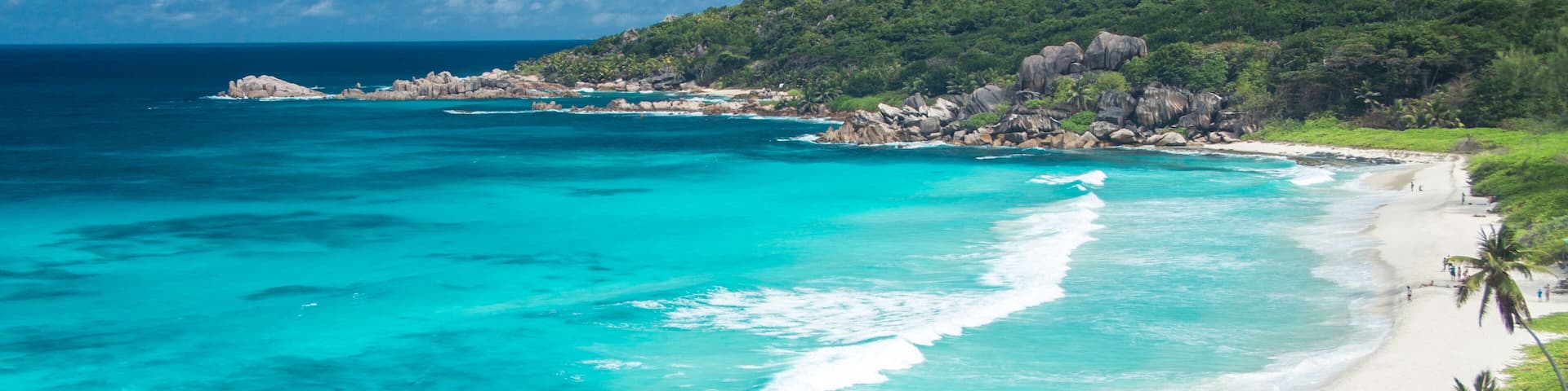 A turquoise beach with white sand, surrounded by lush greenery and rocky outcrops.