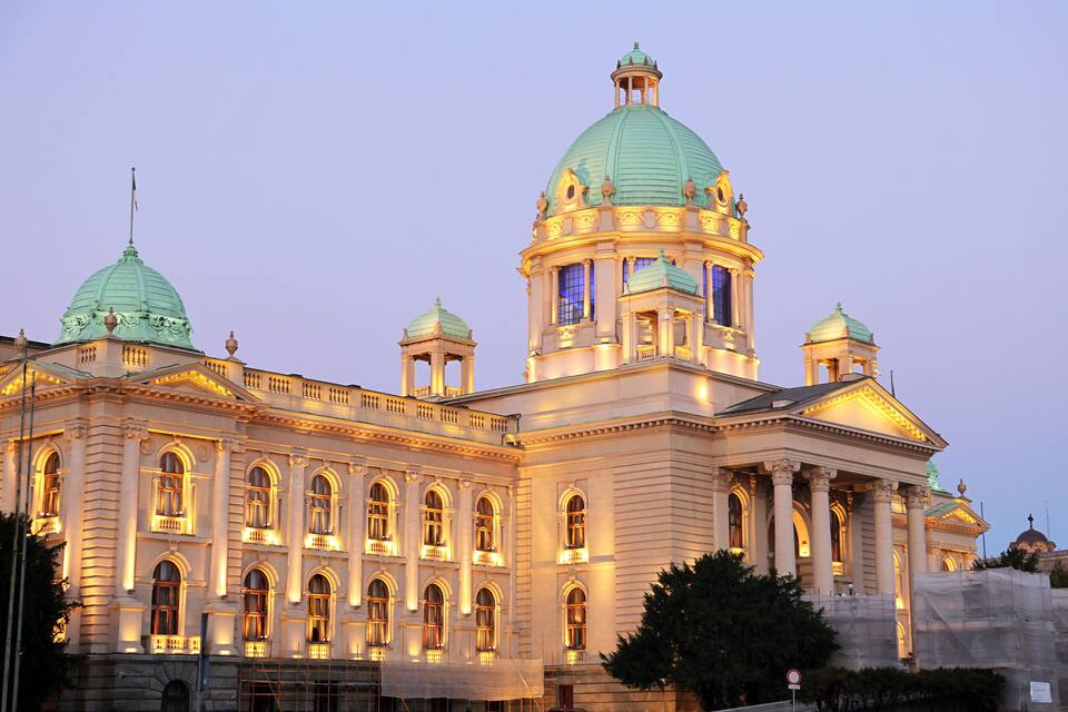 A large, ornate building with multiple domes and columns, illuminated at dusk.