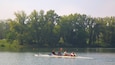 Un equipo de remo en un lago tranquilo bordeado de árboles verdes y frondosos.