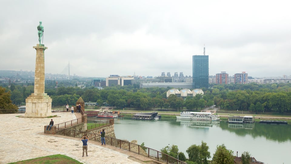 Ein Fluss mit Booten, einer Statue und einer Stadtansicht im Hintergrund.