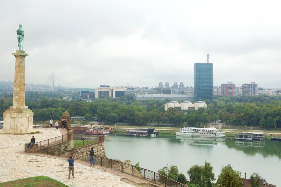 A river with boats, a statue, and a cityscape in the background.