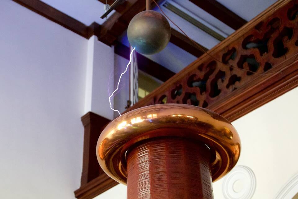 A copper-colored column with a spherical object on top, a wooden beam with a carved design, and a lightning bolt in the background.