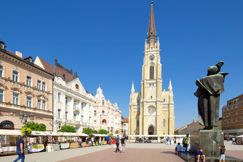Une place historique, dominée par un imposant clocher d’église, une statue et des bâtiments environnants.