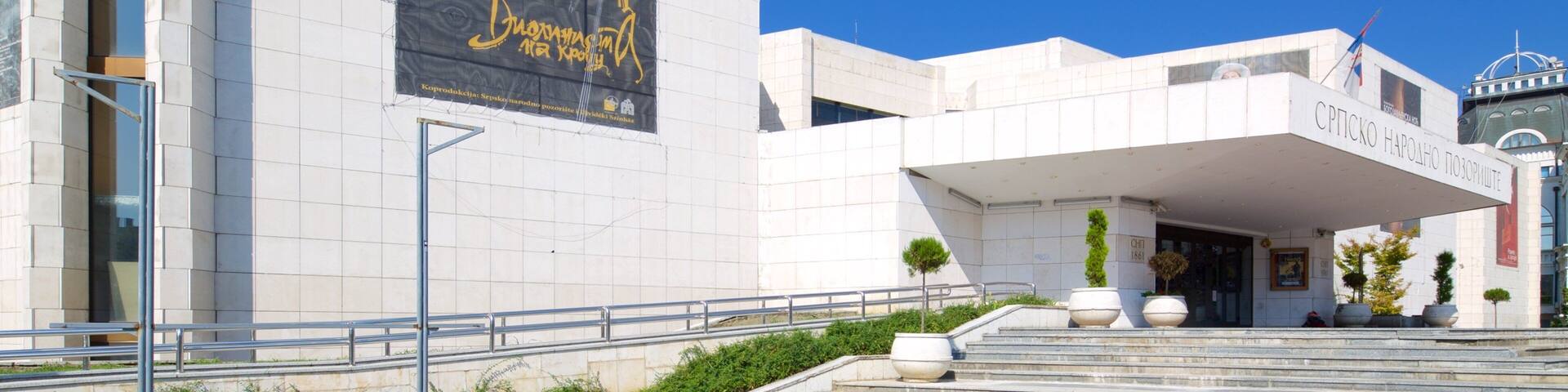 A modern building with a large poster on the side, a clear blue sky, and a flag on top.