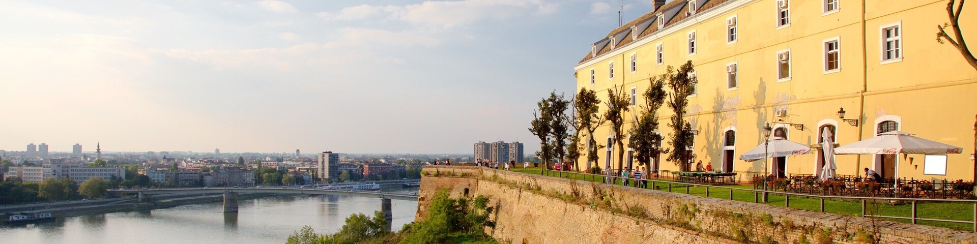 Un río con un puente, un edificio amarillo con terraza y un paisaje urbano al fondo.