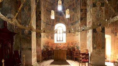 Interior de igreja ornamentado com afrescos, um altar de madeira e uma grande janela em arco.