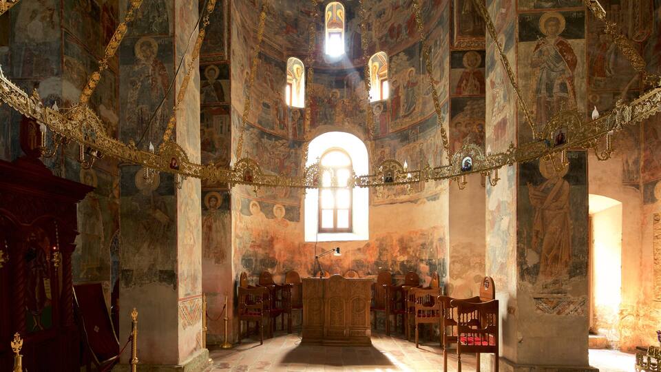An ornate church interior with frescoes, a wooden altar, and a large arched window.