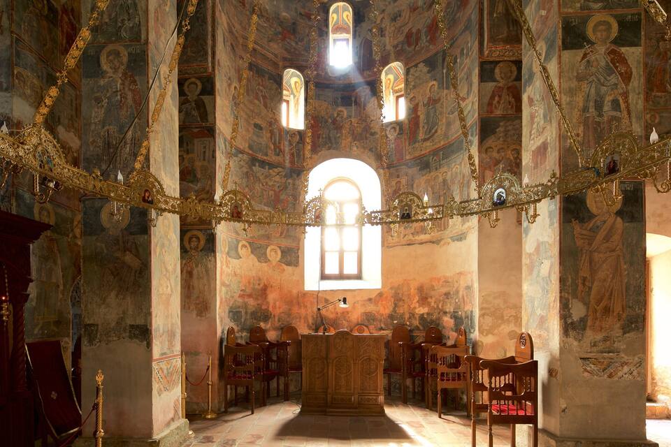 An ornate church interior with frescoes, a wooden altar, and a large arched window.