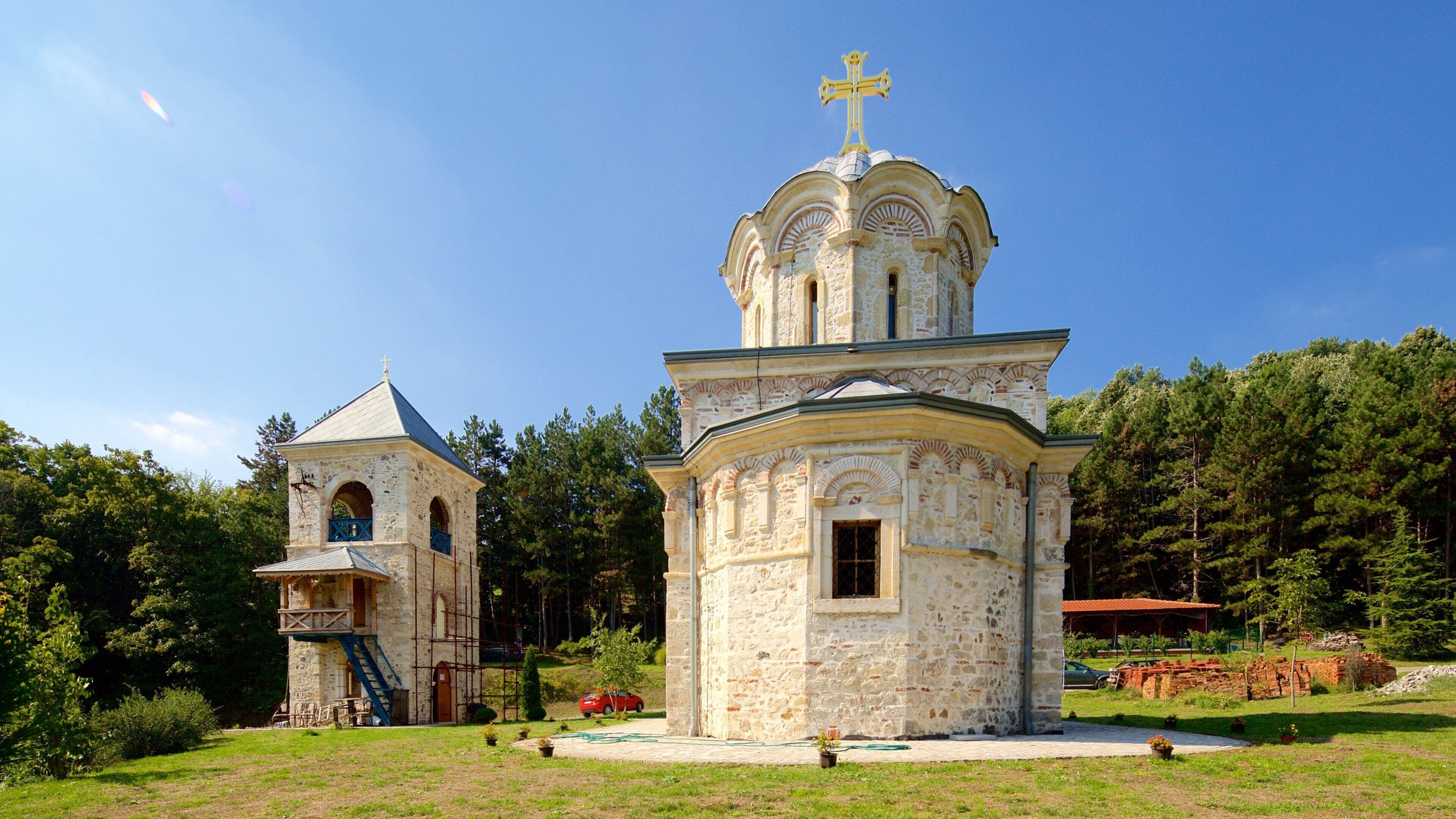 A stone church with a cross on top, surrounded by trees and a clear sky.