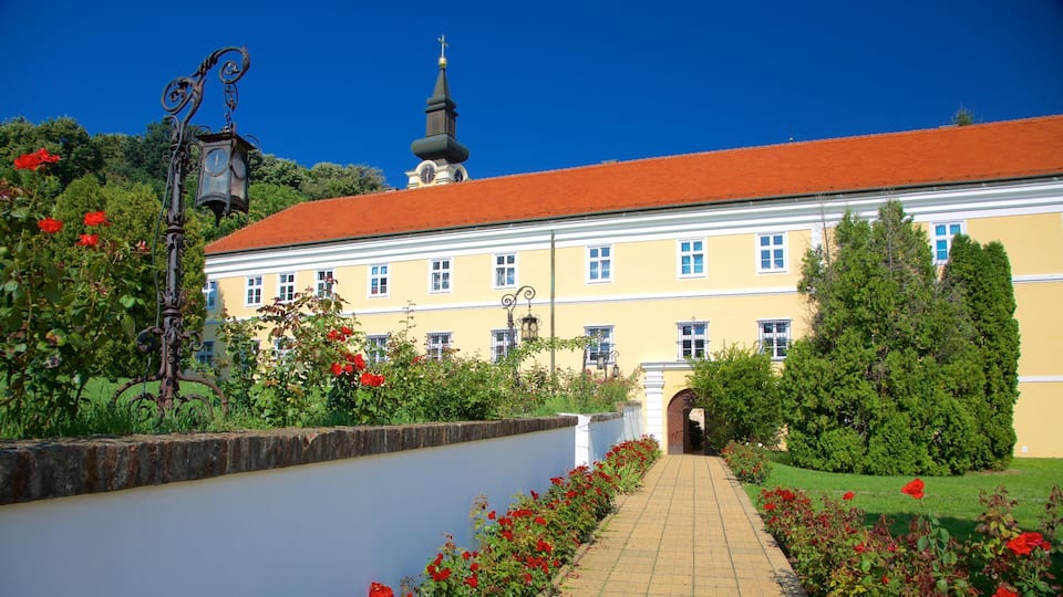 A yellow building with a red roof, surrounded by a garden with red flowers and a pathway leading to a gate.