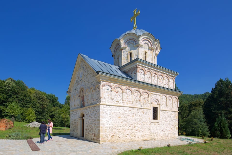 Une petite église en pierre, surmontée d’une croix dorée, entourée de verdure.