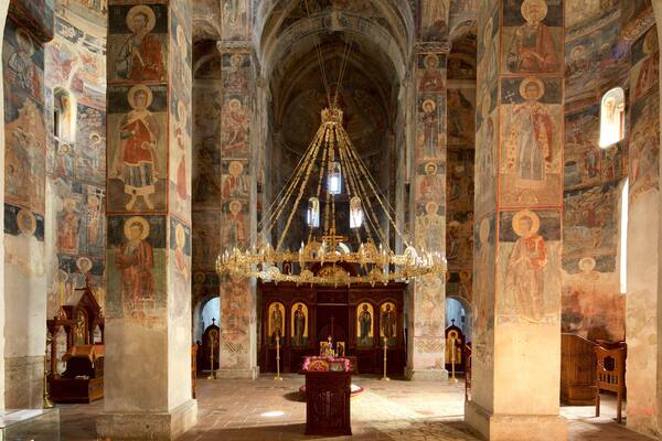 An ornate church interior with a large chandelier, religious icons, and detailed frescoes on the walls.