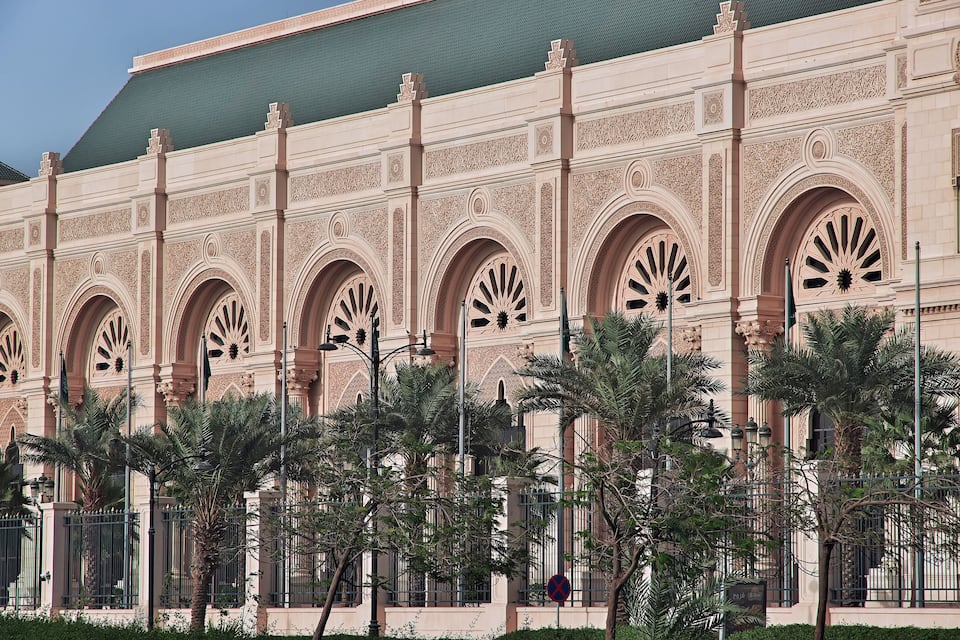A large building with ornate arches and palm trees in front.