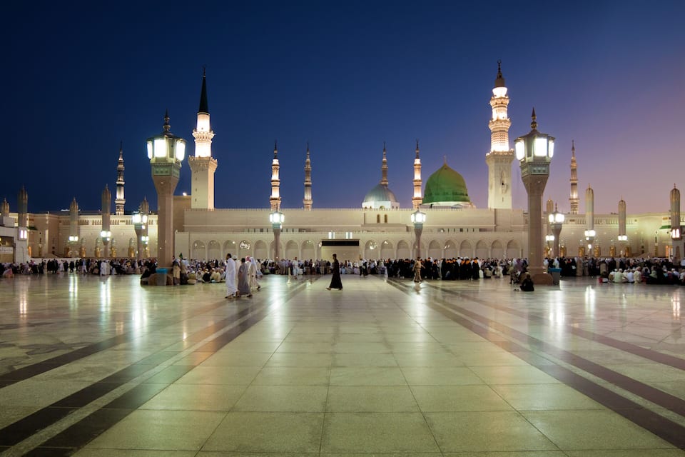 Une grande mosquée dotée de plusieurs minarets et d’un dôme vert, entourée d’une vaste cour où se sont rassemblées de nombreuses personnes.