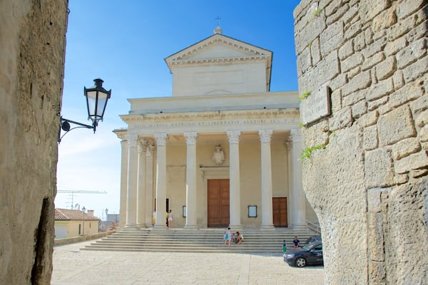 A classical building with columns and a pediment, surrounded by stone walls and a street lamp.