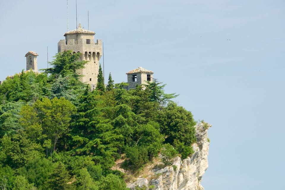 A castle on a cliff surrounded by dense green forest.