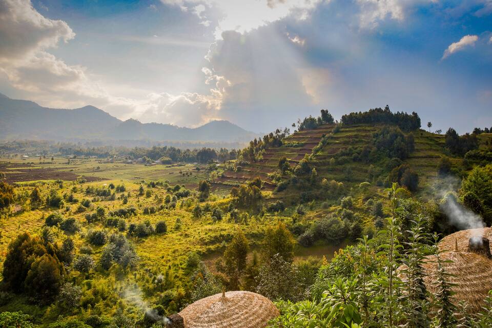Un valle exuberante con campos en terrazas, un río y montañas lejanas bajo un cielo parcialmente nublado.