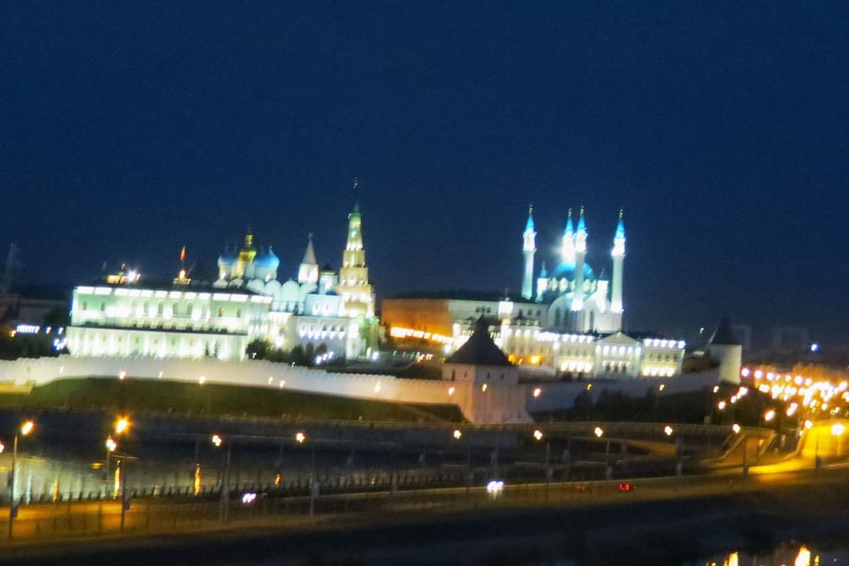 Un grand bâtiment illuminé, doté de plusieurs dômes et de tours, dont le reflet se mire dans une étendue d’eau.