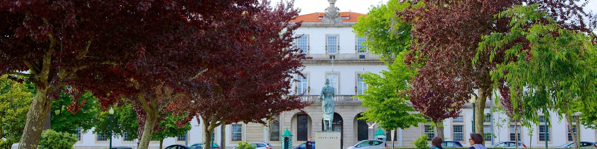 Um parque com bancos, árvores e um edifício com uma estátua no centro.