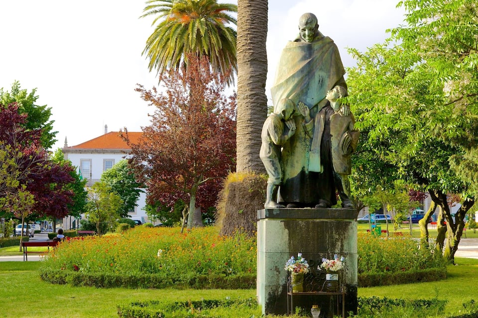 A statue of a man with a child in a park with trees and flowers.