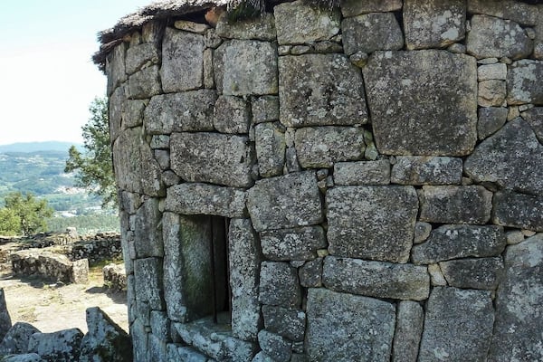 A stone building with a thatched roof, surrounded by a mountainous landscape.