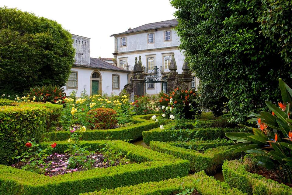 A formal garden with manicured hedges, flowering plants, and a historic building in the background.
