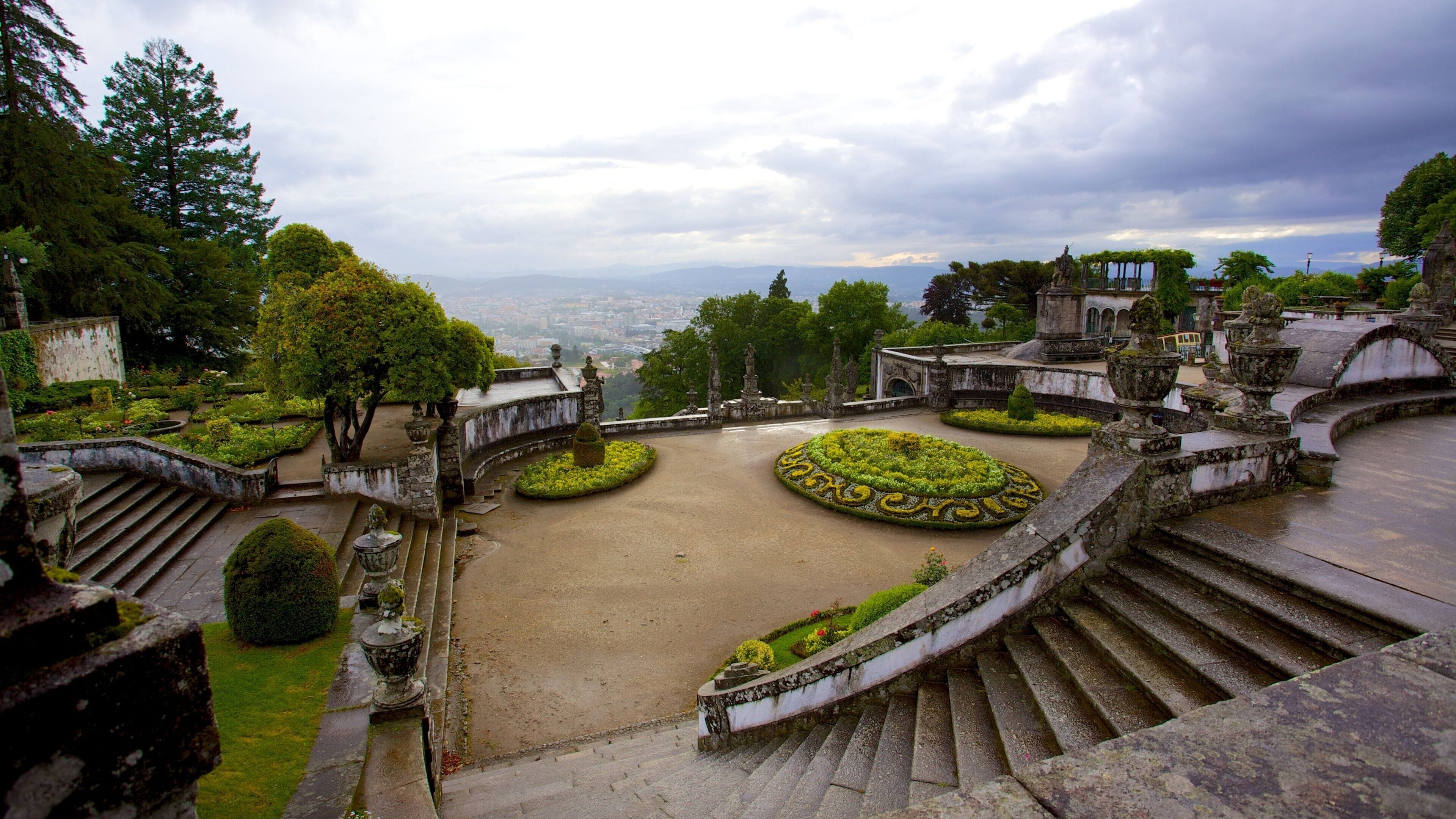 A historic garden with ornate statues, terraced gardens, and a panoramic city view.