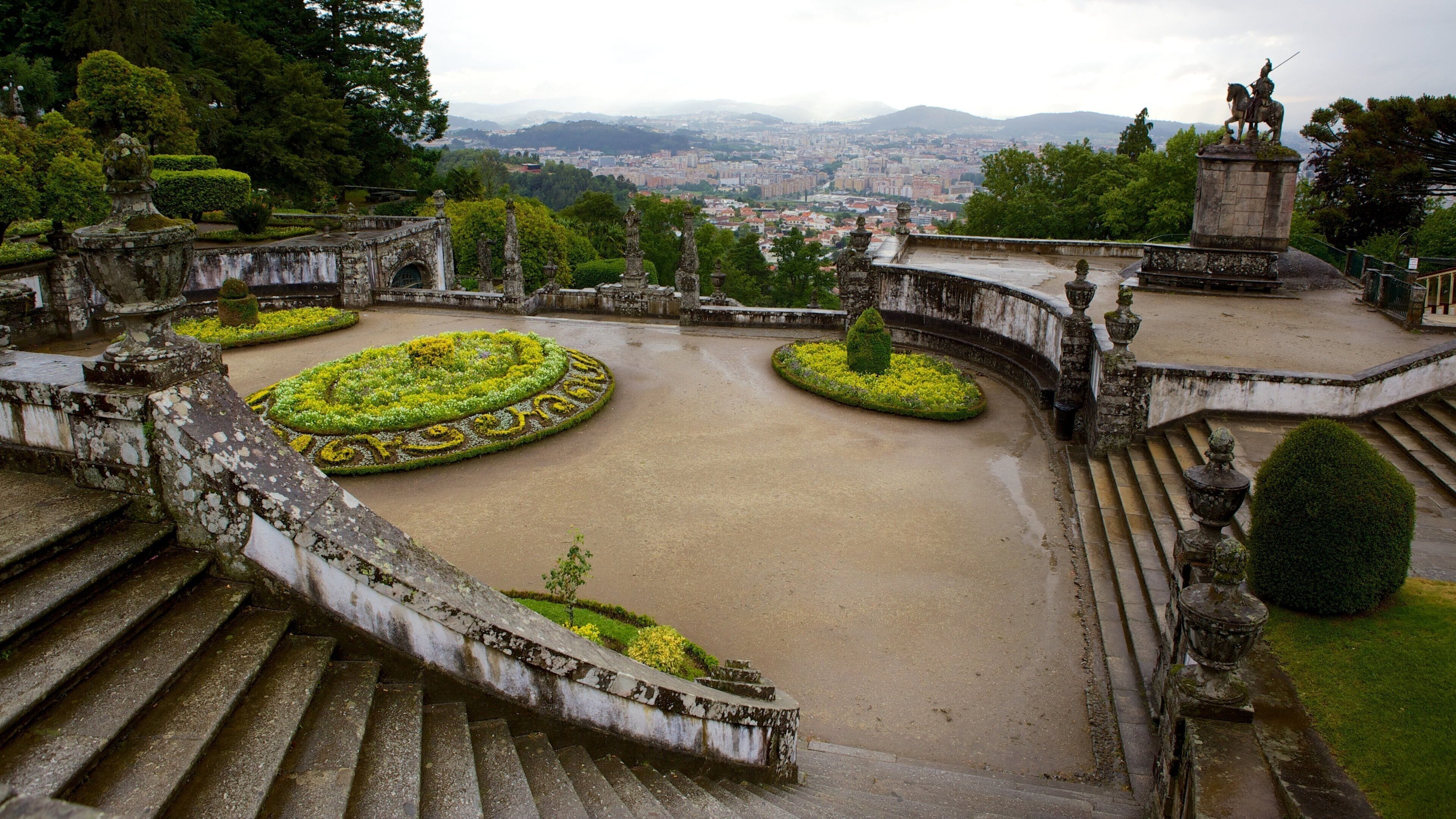 A historic garden with ornate statues, a fountain, and a panoramic city view.