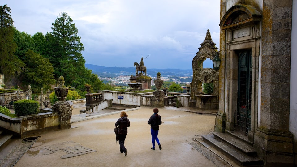 A historic courtyard with statues, a fountain, and a view of a town in the distance.
