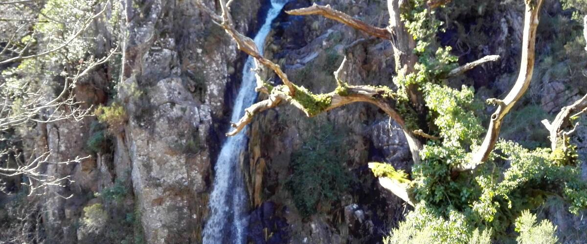 A waterfall cascading down a rocky cliff surrounded by sparse vegetation.