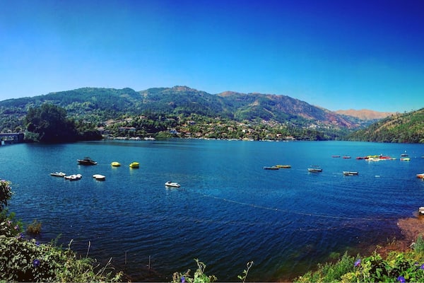 Un lac paisible, avec des bateaux, un pont et des montagnes en arrière-plan.